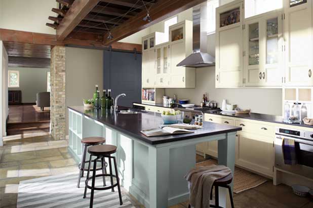 A large, modern kitchen with large island that has dark counters and light cabinets. Backsplash is painted beige. 