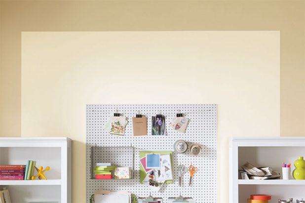A smaller crafting room with shelving and pegboard holding multiple tools and accessories. Walls feature two hues of beige.