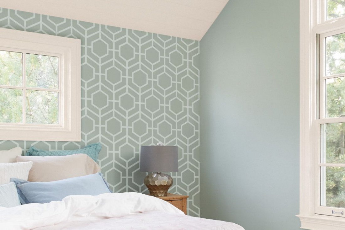 A bedroom features a stenciled geometric pattern in white on a light teal wall.