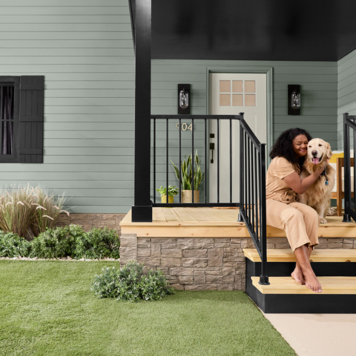 Woman sits on her porch steps, cuddling a golden retriever. The siding of the house is painted Antiquated Pewter. 