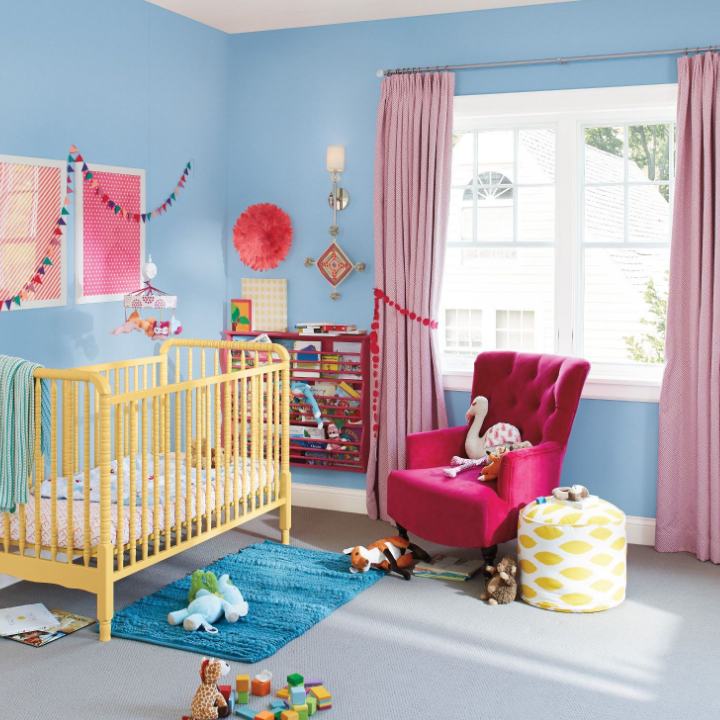 Sunlit nursery room with a yellow crib, majenta accent chair. Nursery is painted the color breezeway.