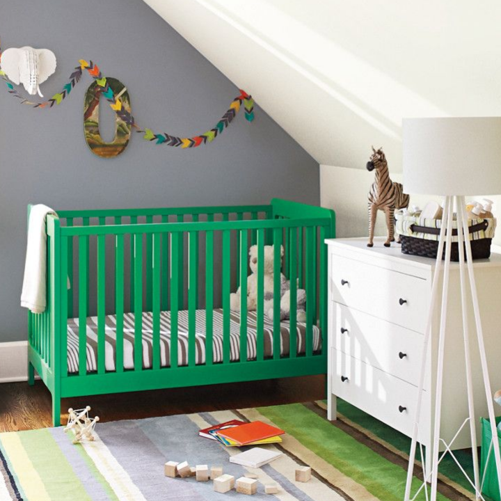A nursery with a green crib, multi-colored rug, with toys strewn about and an over the moon painted wall.