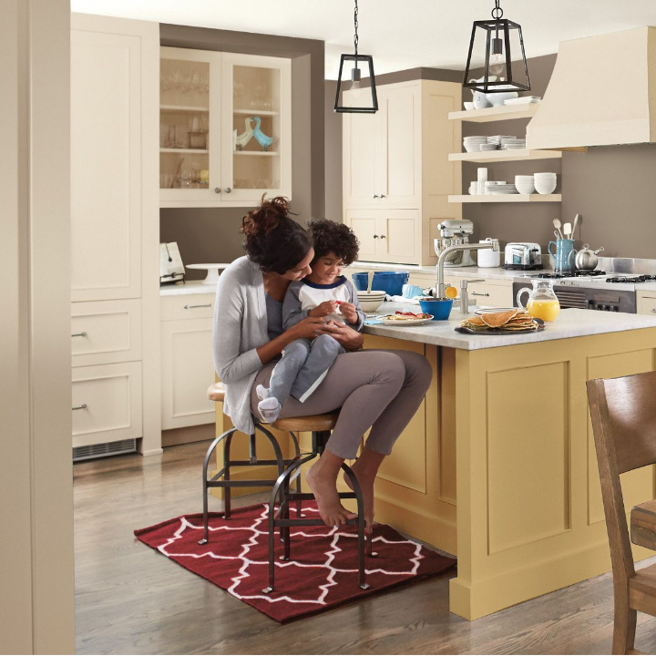 Child sits in his mom’s lap, on a stool at a kitchen counter with breakfast served. 