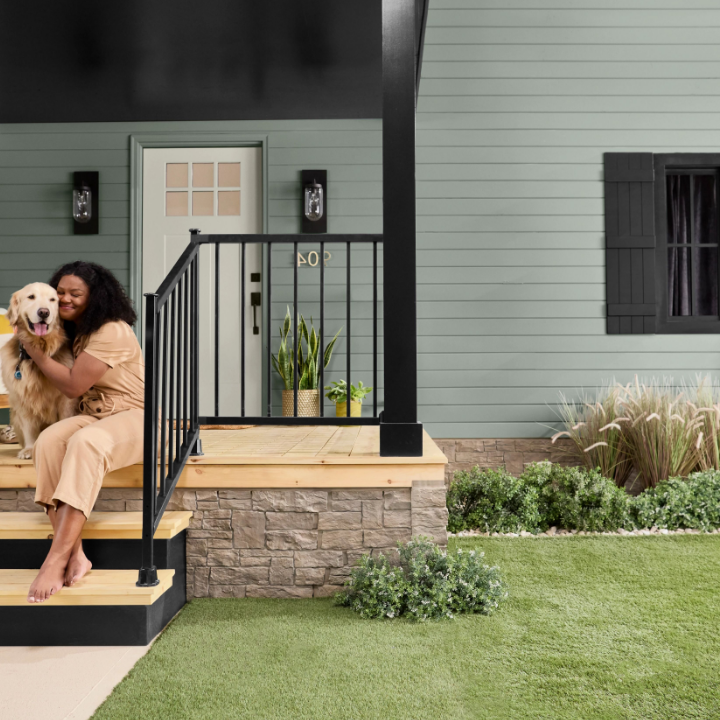 Woman sits on porch steps with her golden retriever. The exterior of the house is painted the color Antiquated Pewter.