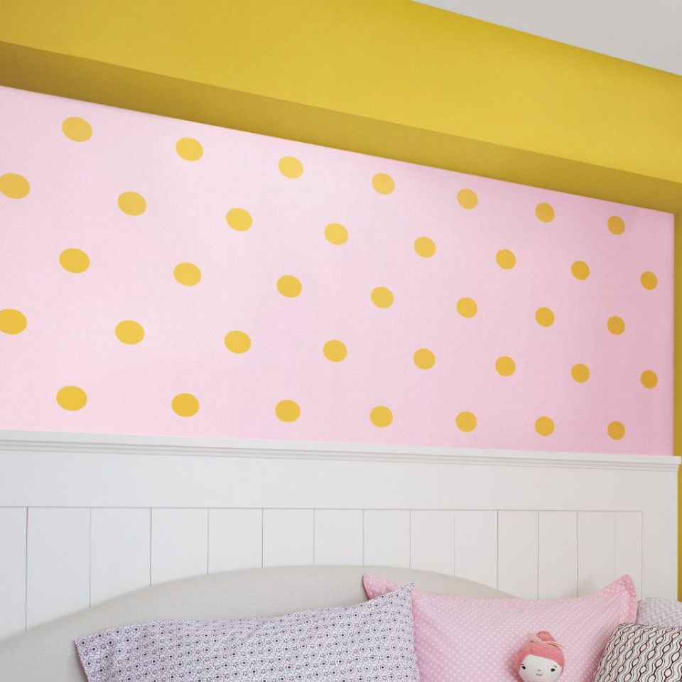 A child’s room with a polka dot print on the wall and a bed. Upper wall is painted yellow.
