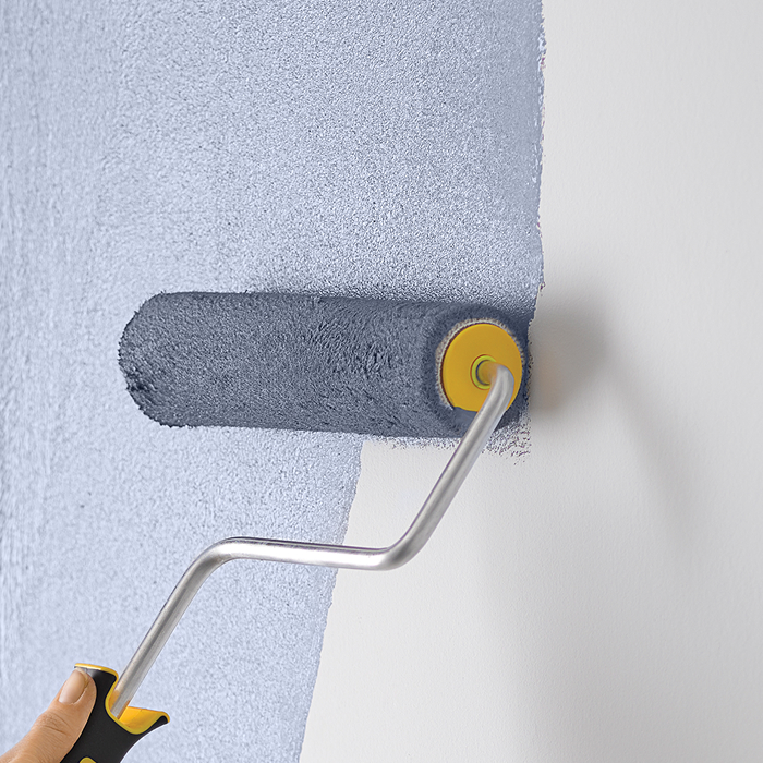 Paintroller covered in aqua paint, rolling paint onto a white wall.