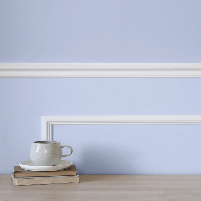 Wall painted light blue with decorative molding in white, in foreground coffee cup resting on two books.
