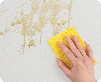 Person wiping coffee stains from a white wall, showing clean surface being left behind.