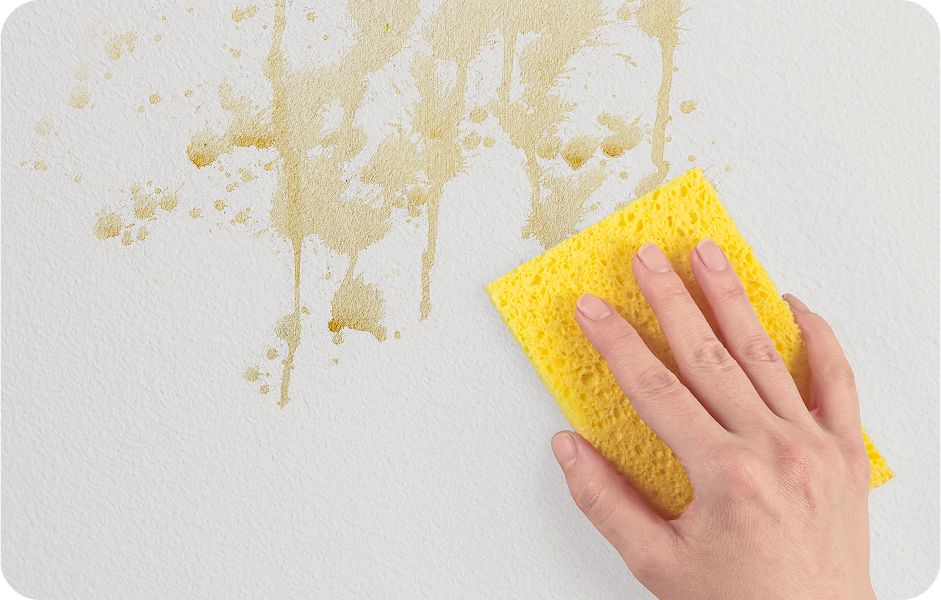 Person wiping coffee stains from a white wall, showing clean surface being left behind.