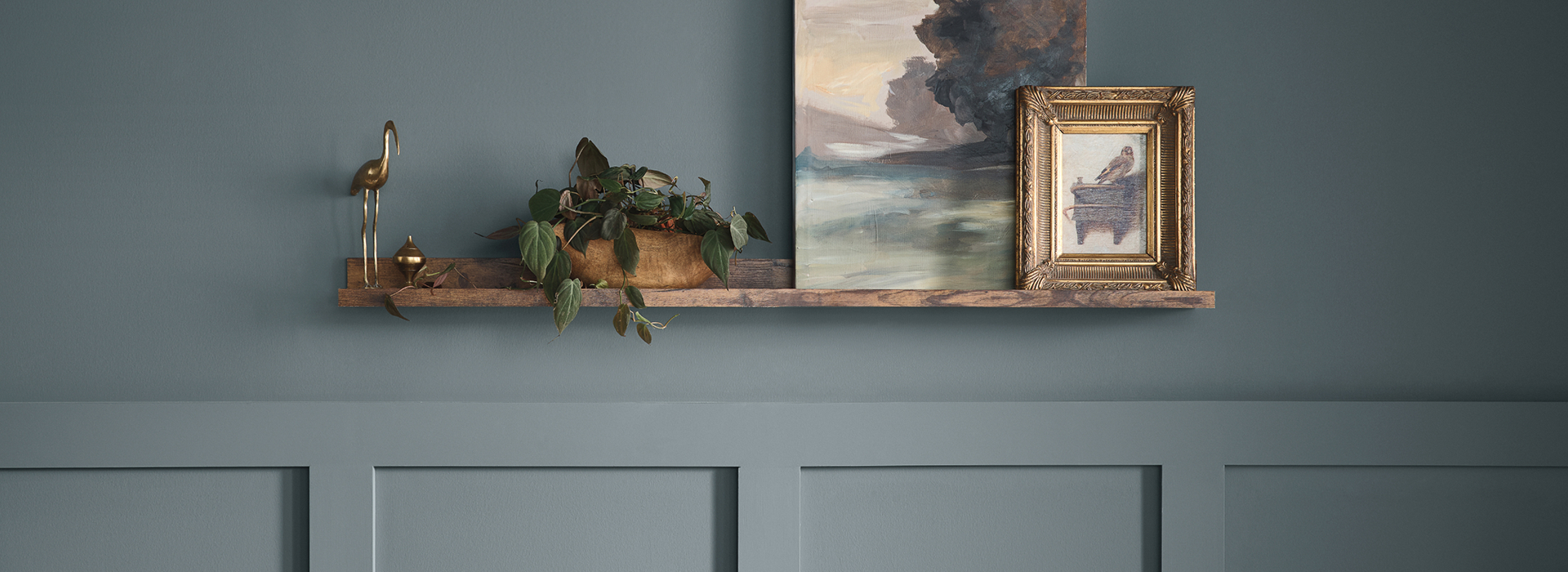 Detail of a beautifully-styled room in muted blue tones featuring a wooden shelf with framed artwork, plants and decor.
