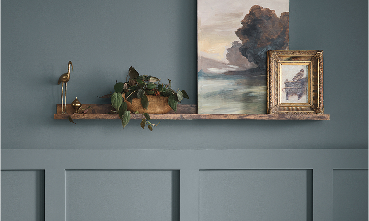 Detail of a beautifully-styled room in muted blue tones featuring a wooden shelf with framed artwork, plants and decor.