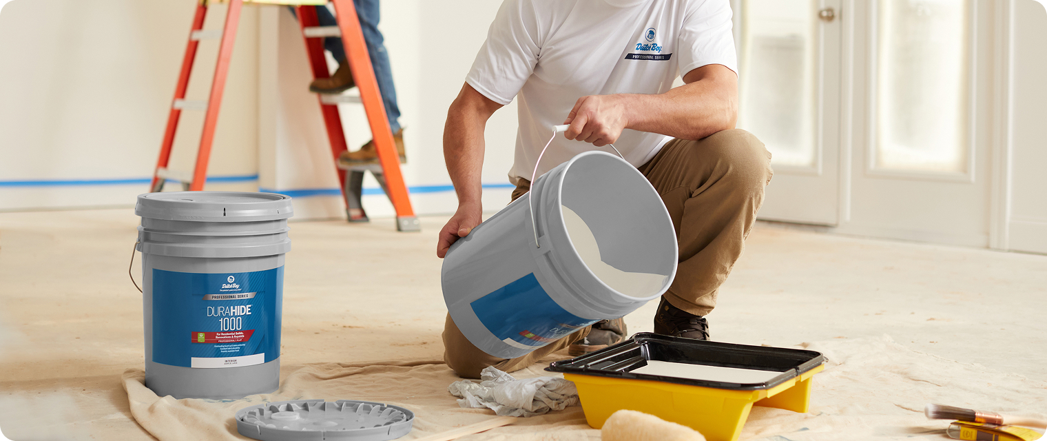 Paint Pro pouring a 5 gallon bucket of paint into a paint tray
