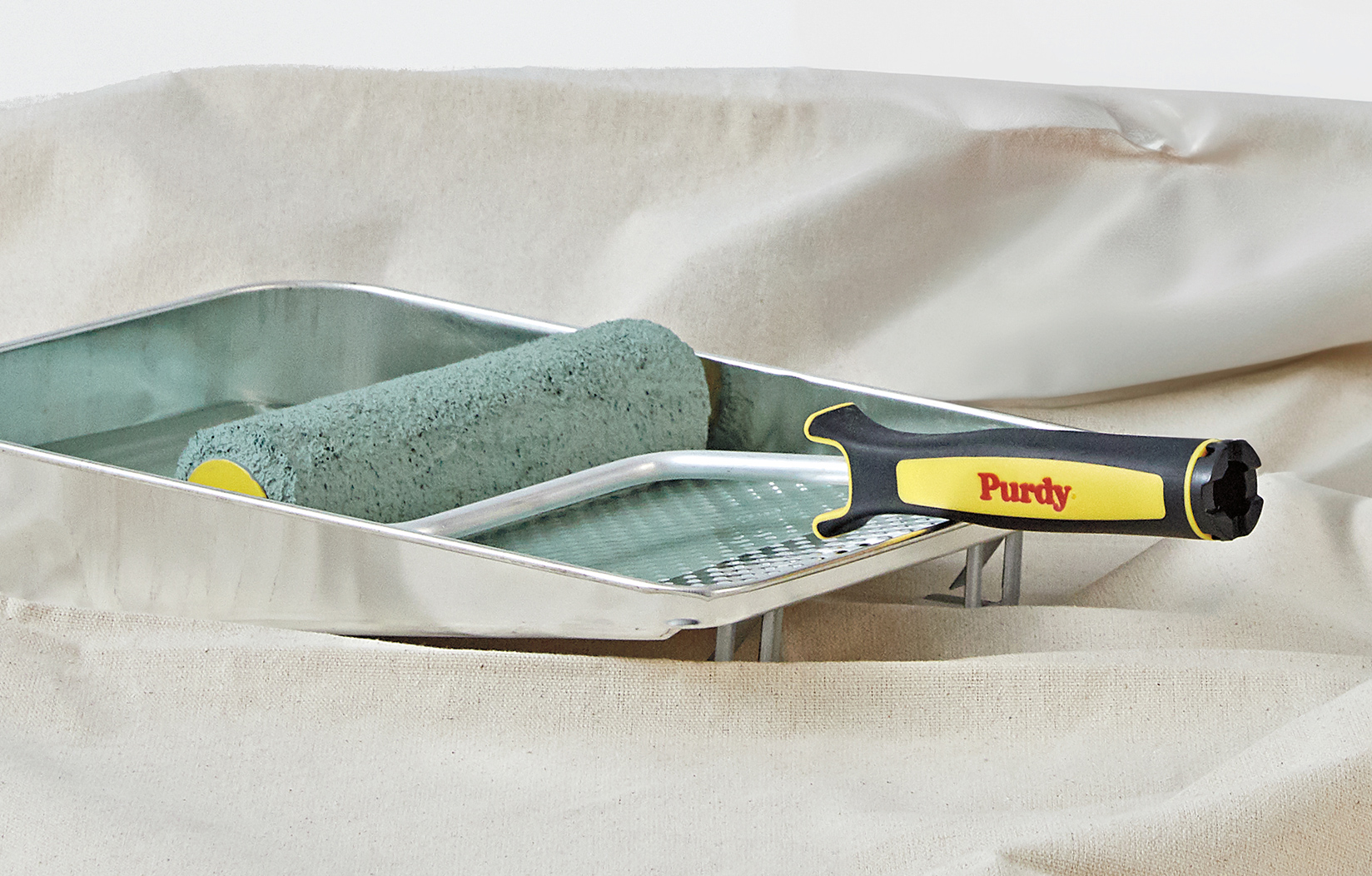 Green paint in a paint tray, on top of a tarp with a Purdy paint roller