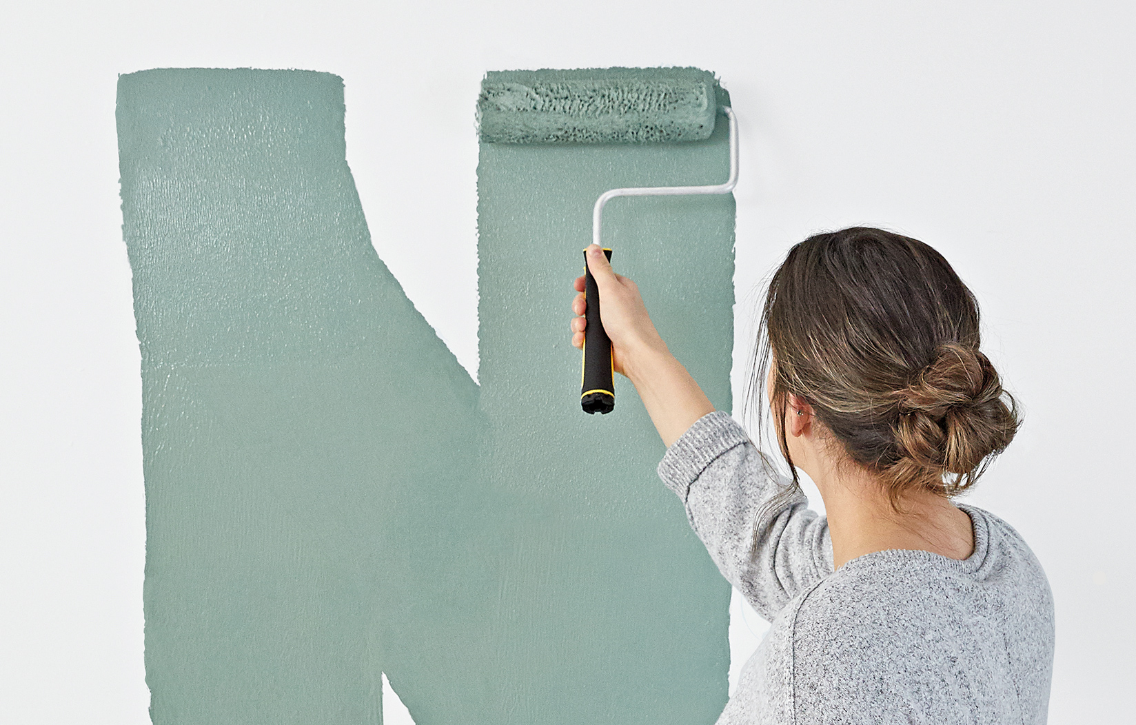  A woman applies green paint to a white wall with a paint roller.    