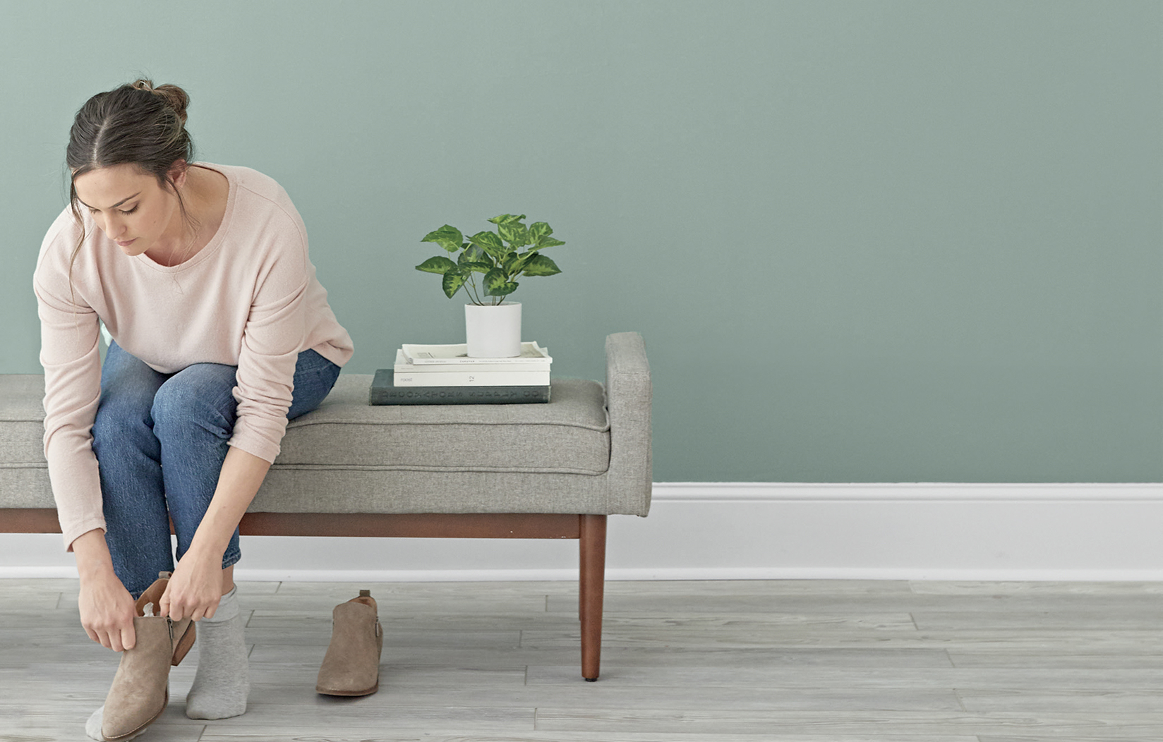 A woman sits on a padded bench adjusting her shoe in her newly painted room.