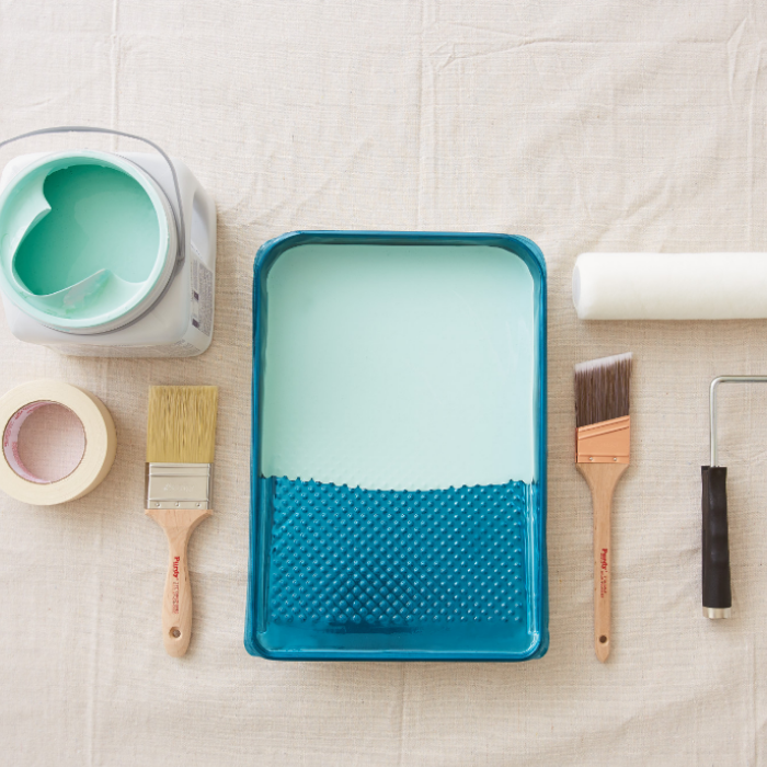  Overhead shot of paint cans, painter’s tape, paintbrushes, tray and roller on a paint tarp.