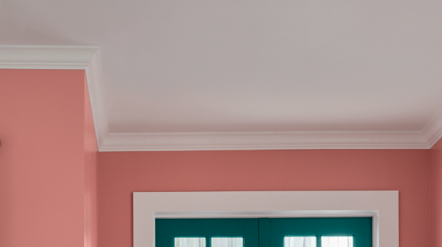 Home entryway-only visible things are the top of deep teal French doors, a pink wall and a white ceiling with crown molding.