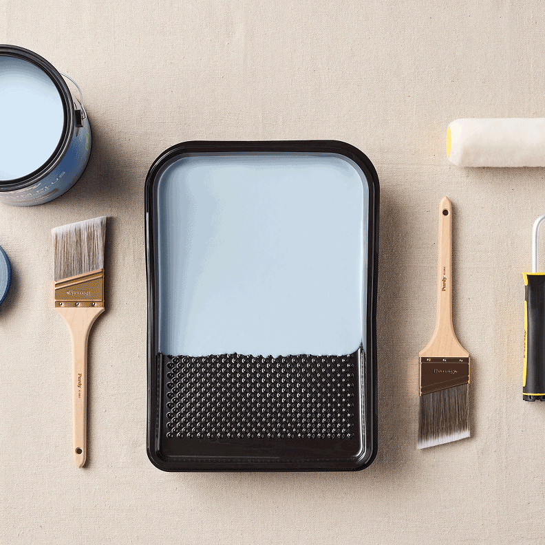 Overhead shot of a paint can, paintbrushes, tray and roller on a paint tarp.
